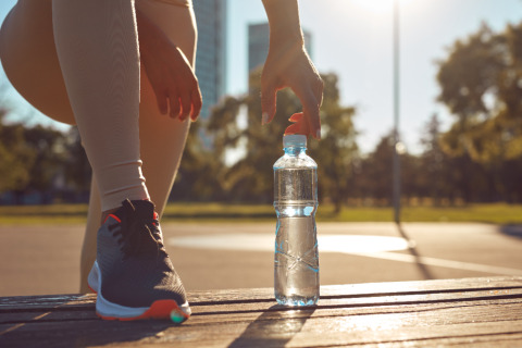 Young attractive sporty woman making pause for tying shoelaces and drink water during exercising in the park.
